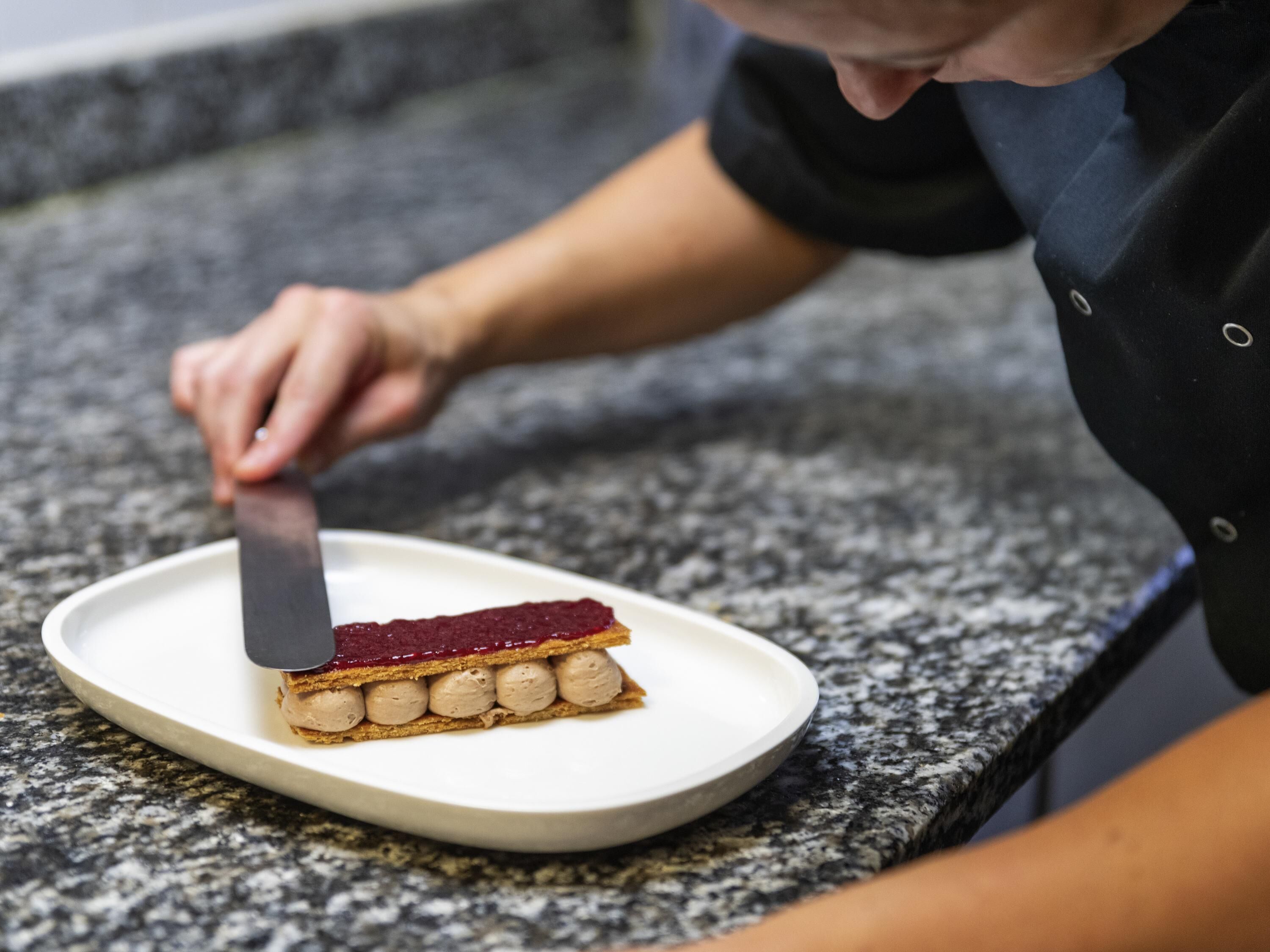 A person cutting a layered dessert on a white plate.