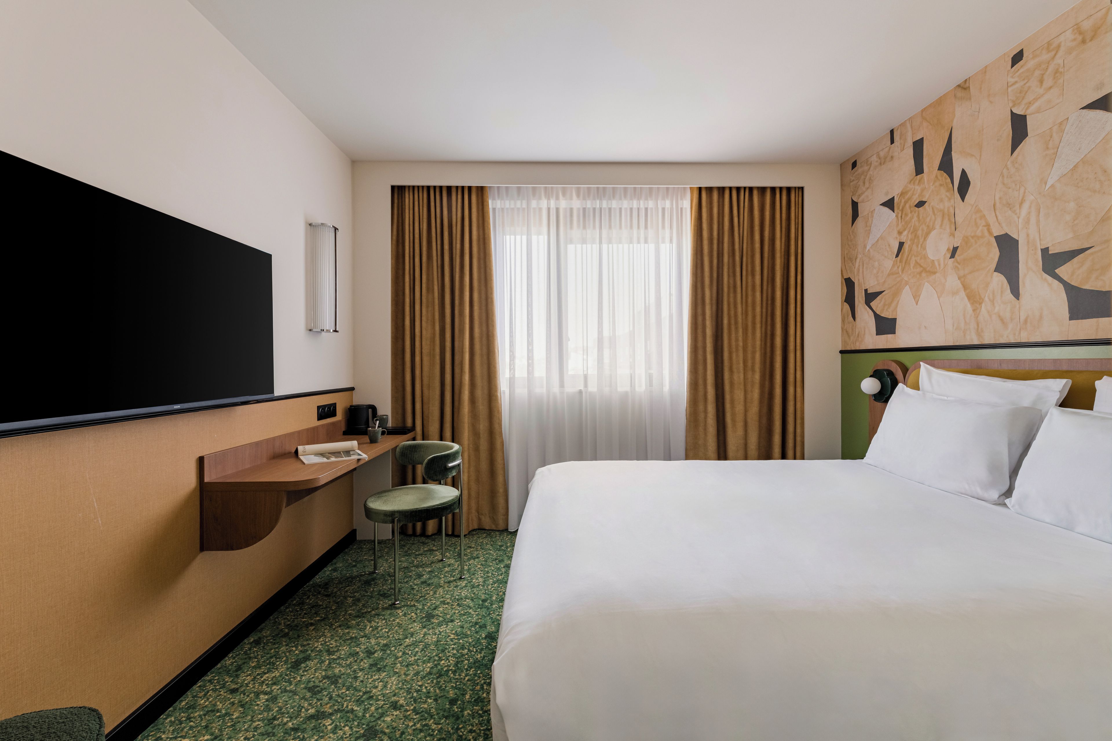Habitación de hotel con cama, escritorio, silla, televisor y ventana con cortinas.