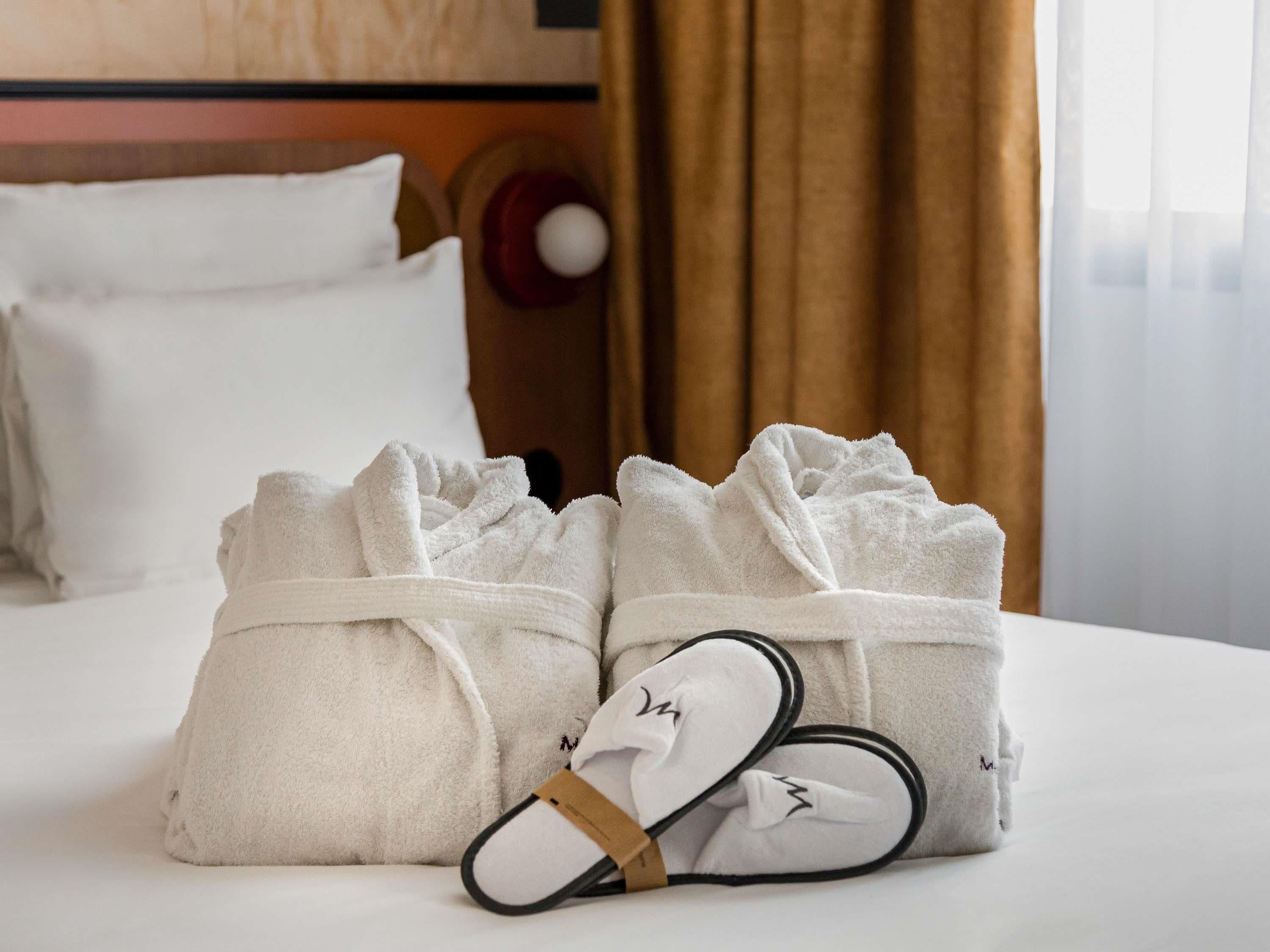 Una cama bien tendida con sábanas blancas, un par de pantuflas y una bata doblada sobre una cama de hotel.