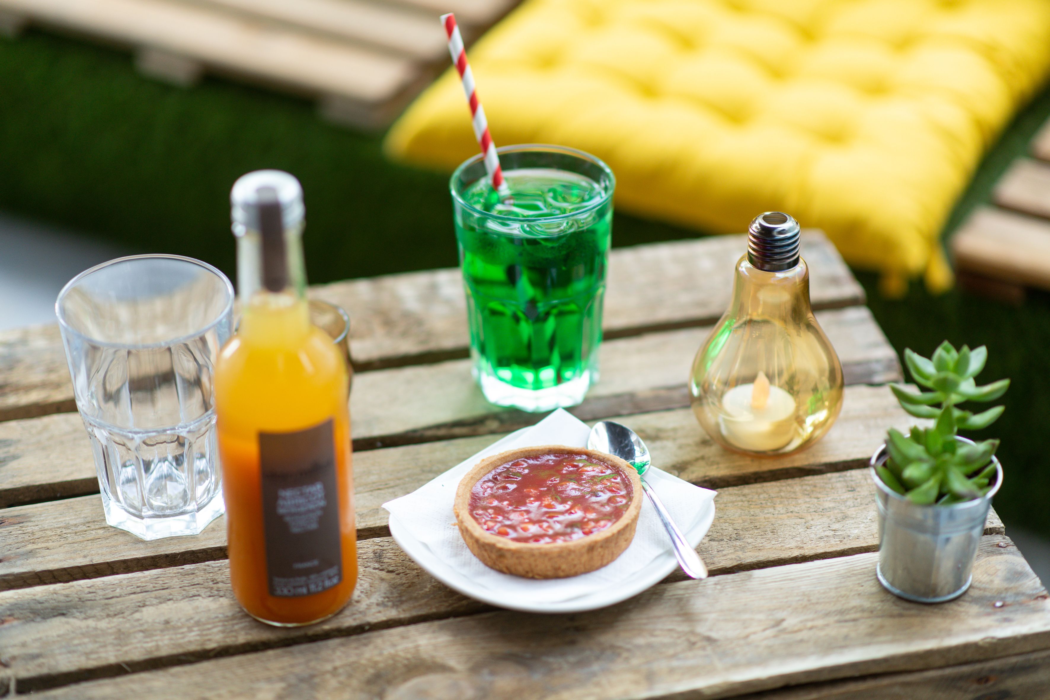 A wooden table with a glass of orange juice, a bottle of water, a green drink with a straw, a small candle, and a succulent plant.