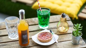 A wooden table with a glass of orange juice, a bottle of water, a green drink with a straw, a small candle, and a succulent plant.