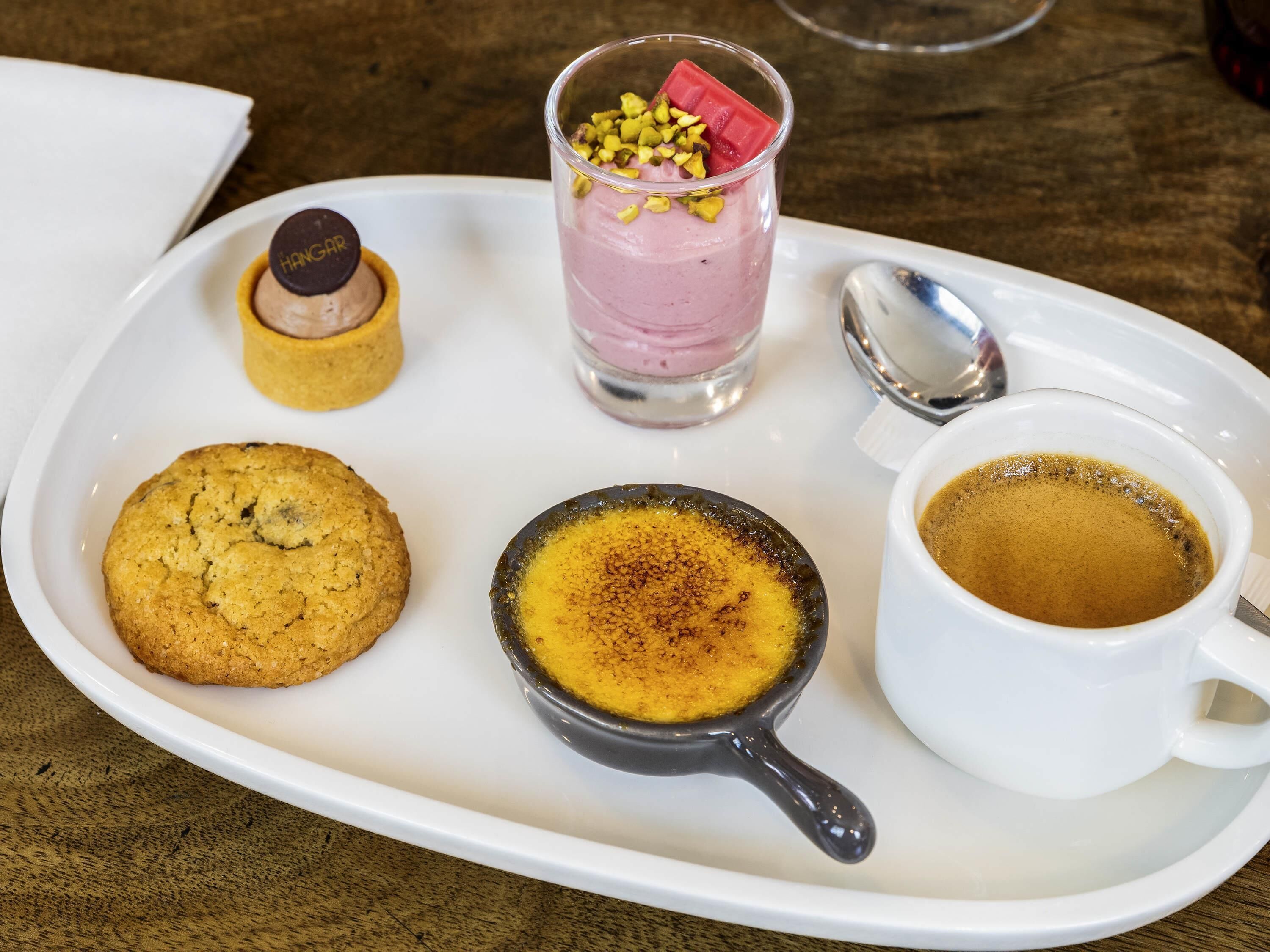 Una bandeja con un postre, un vaso de smoothie, una galleta, una taza de café y un bombón de chocolate.