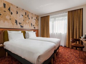 A hotel room with two beds, a desk with a chair, a large window with curtains, and a wall with a geometric pattern. - Hôtel Mercure Lyon Centre Lumière (Lyon)