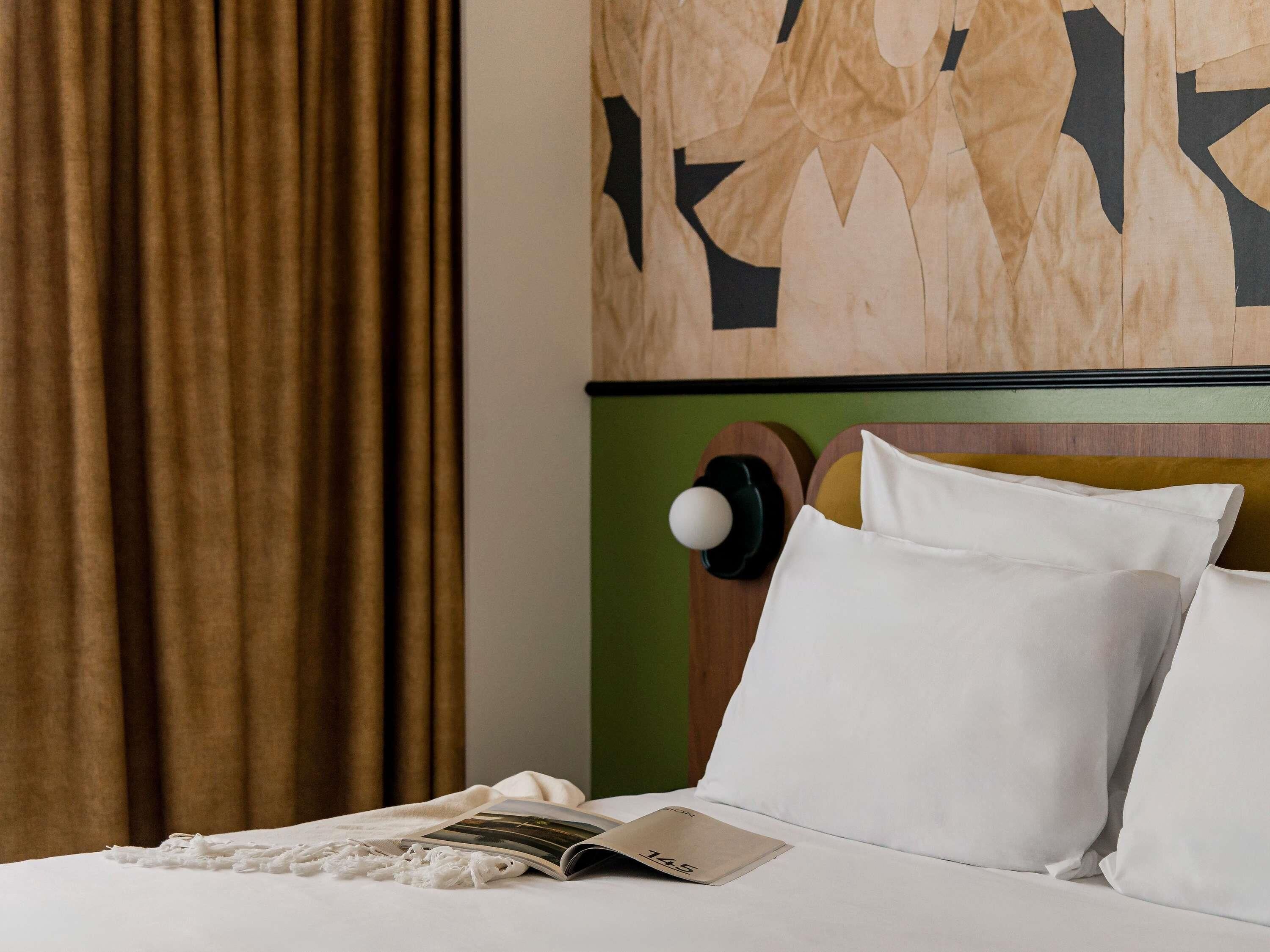 A neatly made bed with white bedding, a magazine, and a pillow with a number on it.