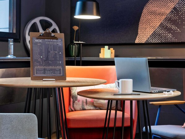 Un café moderno con una pizarra de menú, una computadora portátil, una taza blanca y un área de estar acogedora con un cojín rojo.