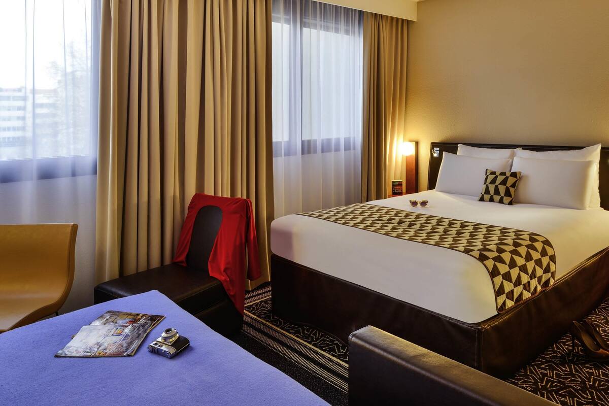 A hotel room with a bed, a chair, a table, and a window with curtains.