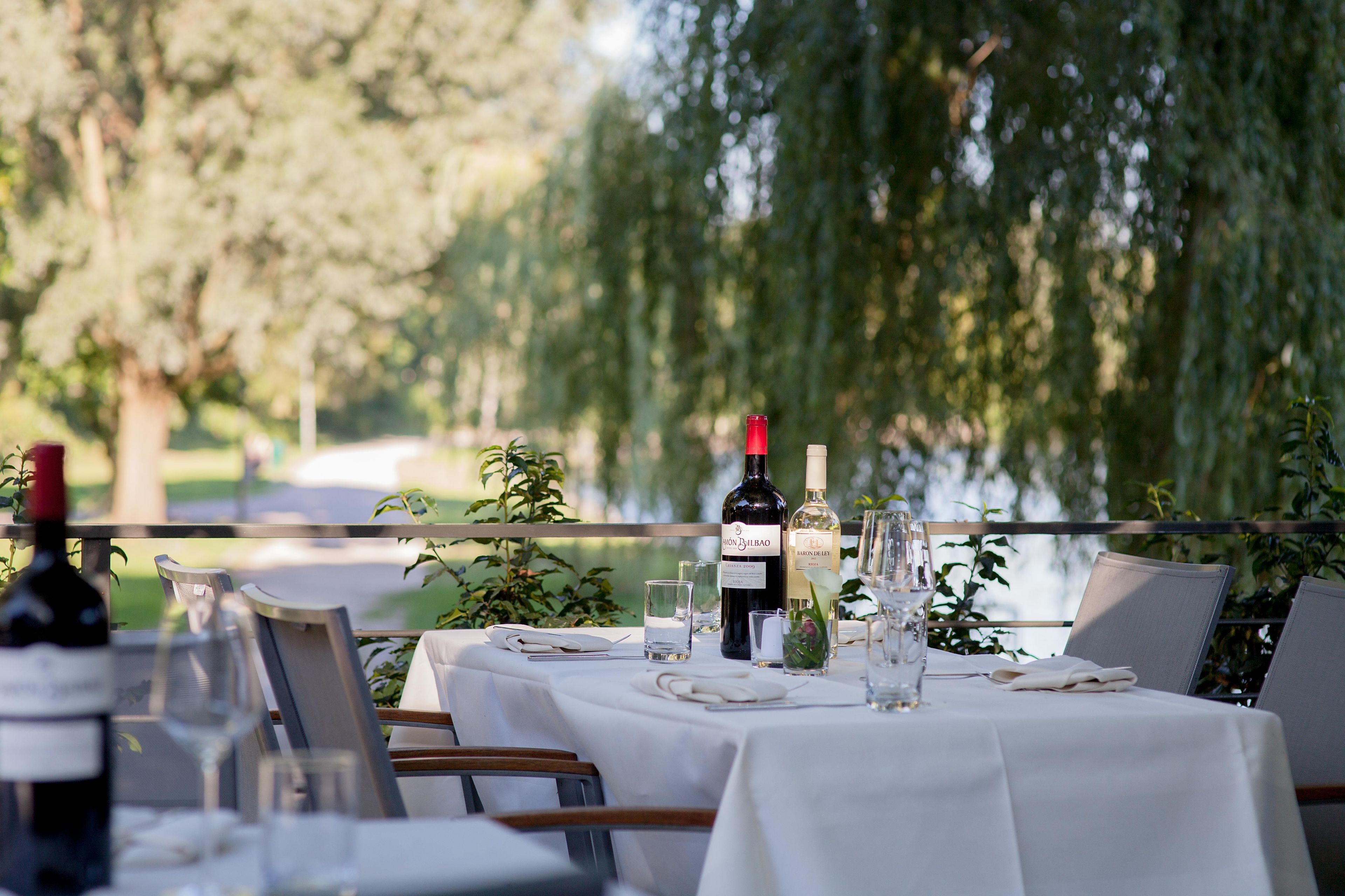 An outdoor dining area with tables set for a meal, overlooking a body of water.
