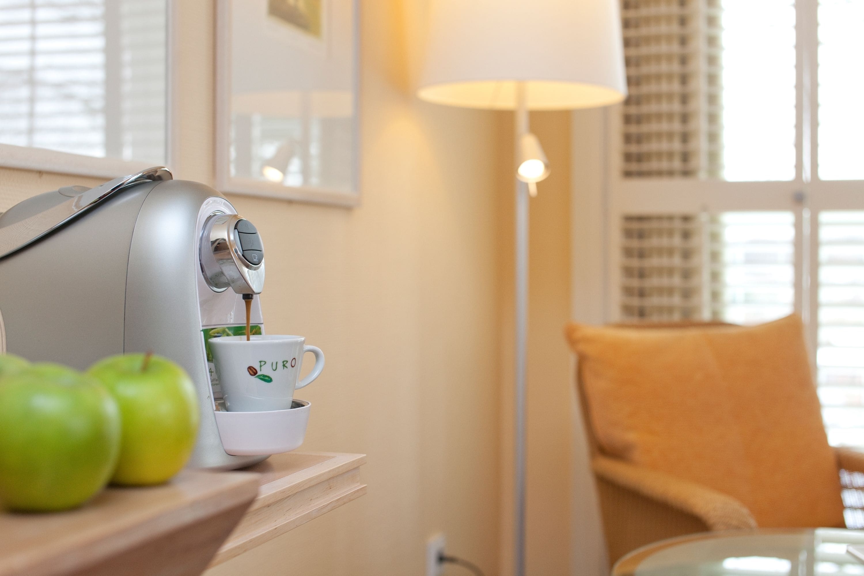 A coffee maker on a table with a cup and apples.