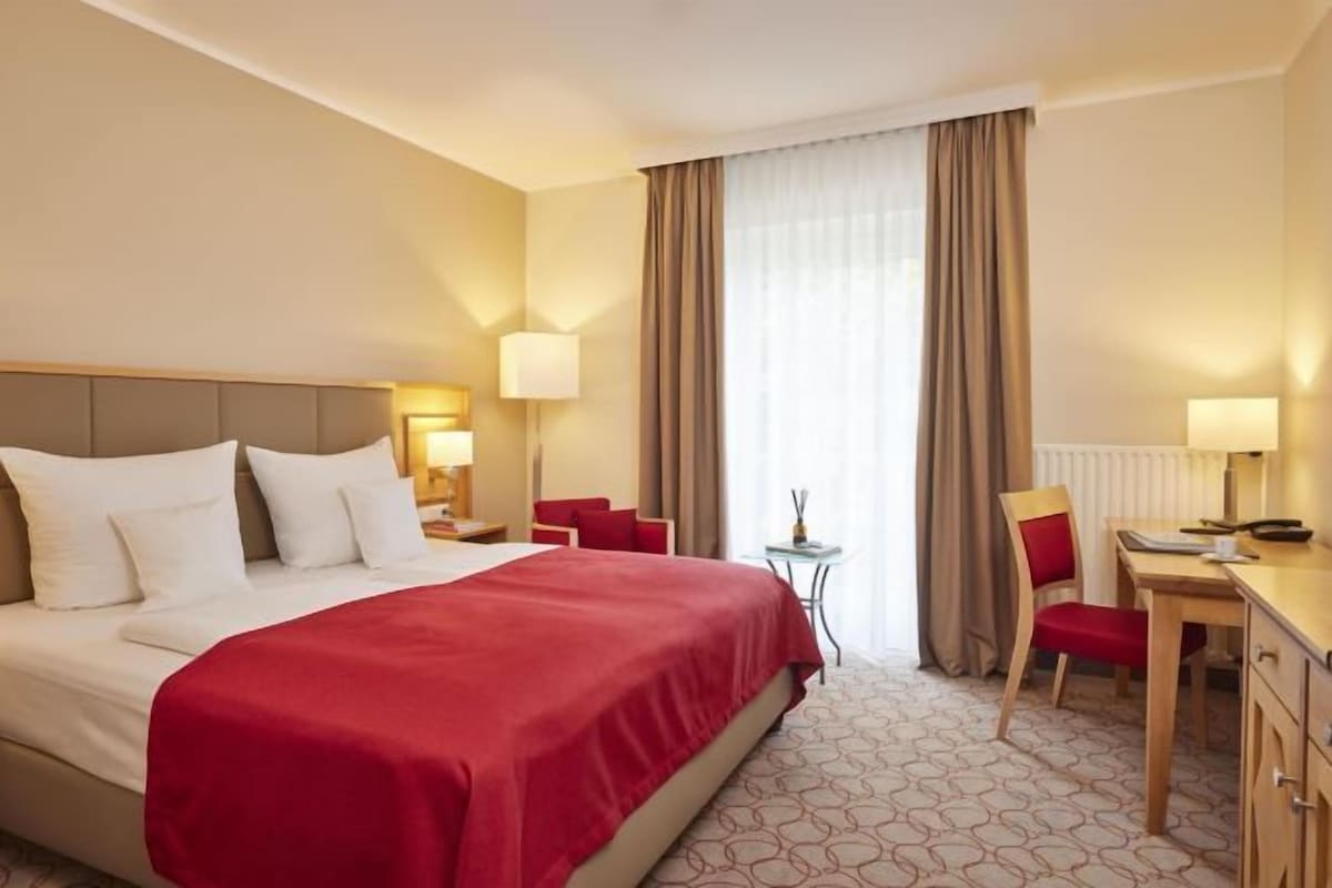 A hotel room with a large bed, a desk, a chair, and a small table.