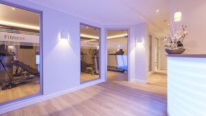 Un centre de remise en forme moderne avec des murs recouverts de miroirs, du matériel d’exercice et un plancher en bois.