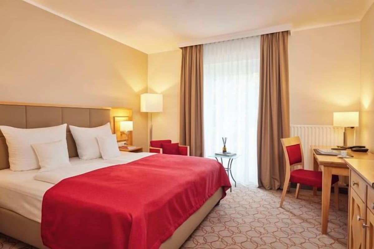 A hotel room with a large bed, a desk, a chair, and a small table.