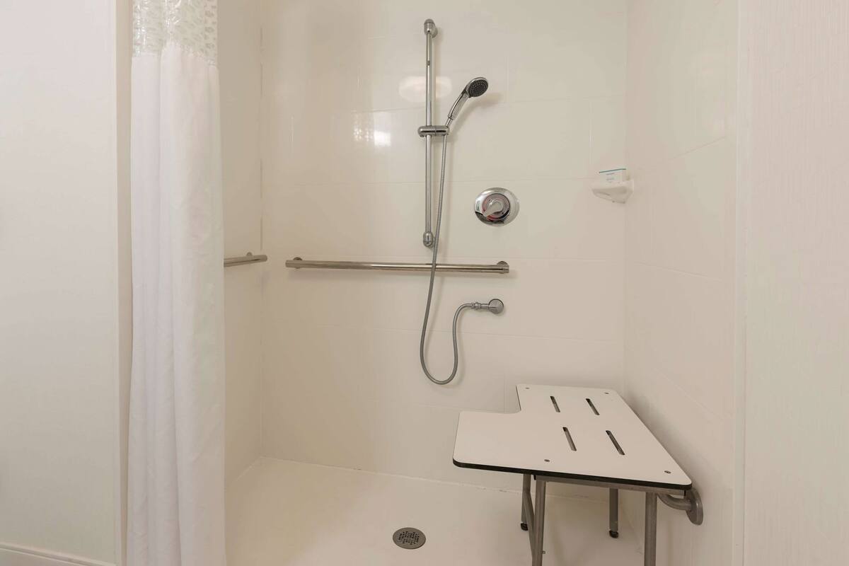 A shower with a handheld showerhead, a wall-mounted faucet, and a small table with slots.