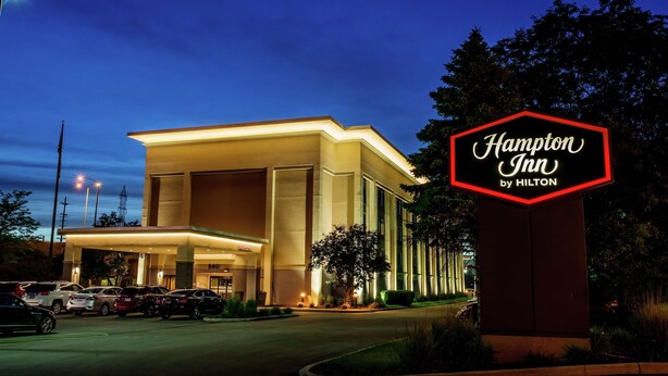 Un hotel Hampton Inn by Hilton al atardecer, con una entrada bien iluminada y un estacionamiento.