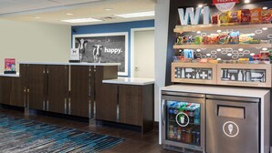 Un área de recepción con mostrador, un refrigerador con bebidas y estantes con aperitivos.