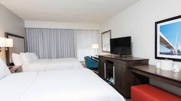 A hotel room with two beds, a desk with a TV, a chair, and a red bench.