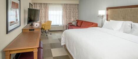 Habitación de hotel con cama, escritorio, televisión, silla y ventana con cortinas.