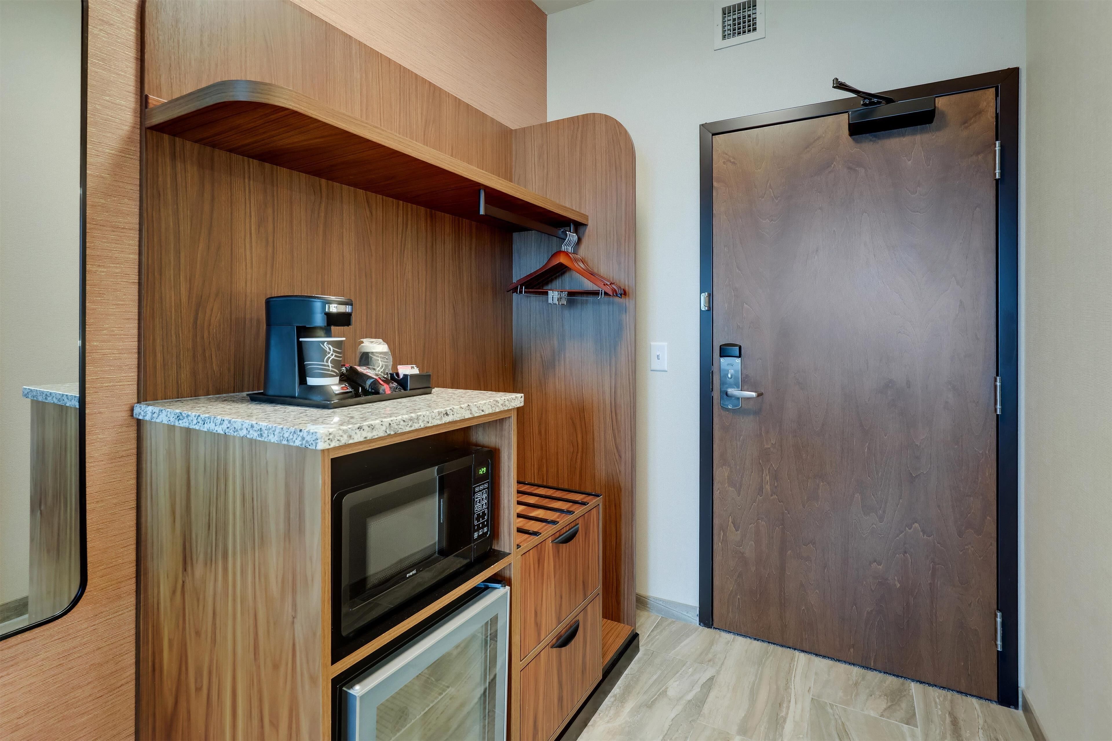 Una kitchenette compacta con microondas, cafetera y un refrigerador pequeño.
