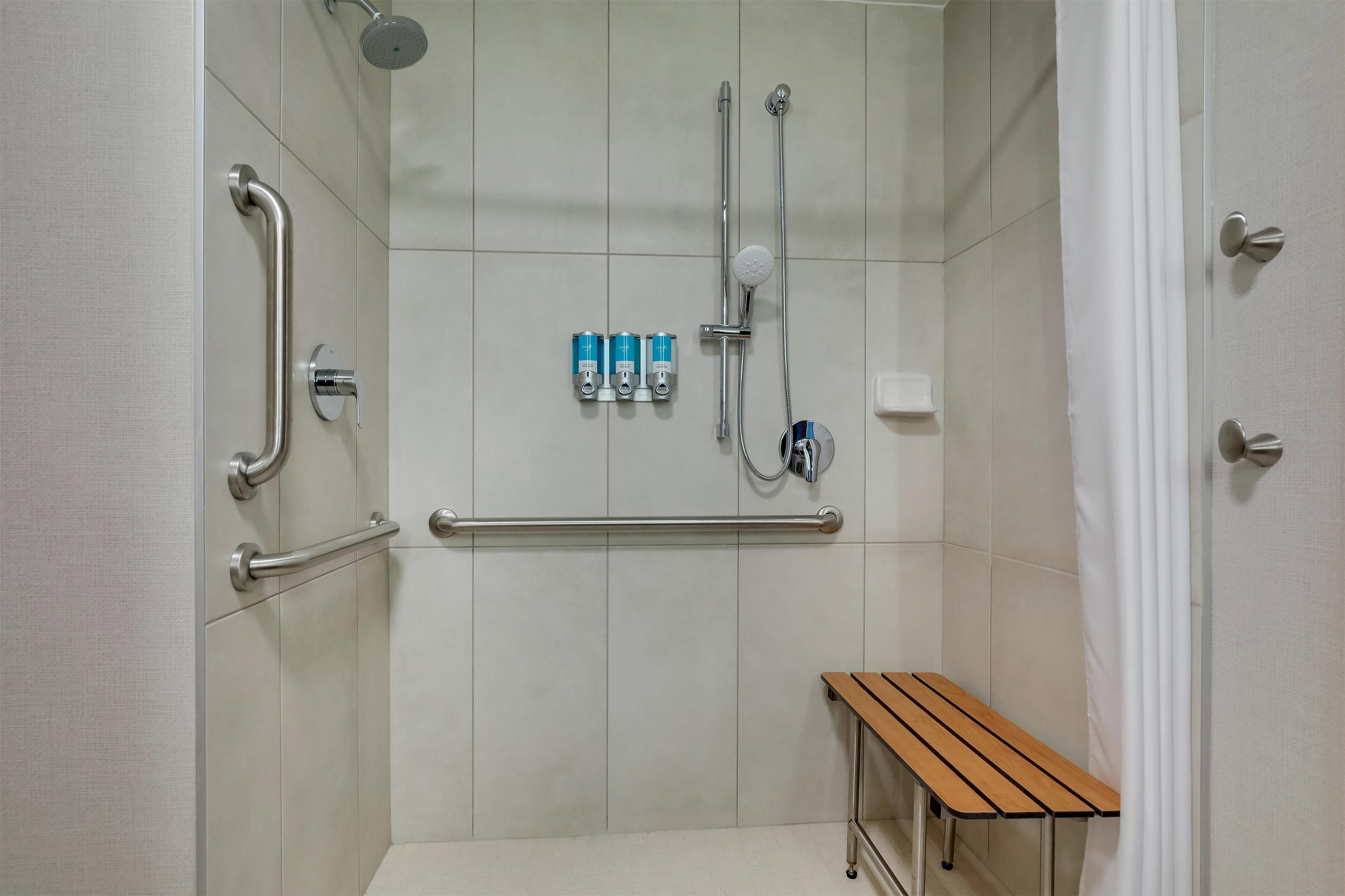 A bathroom with a shower, grab bars, a bench, and a hand dryer.