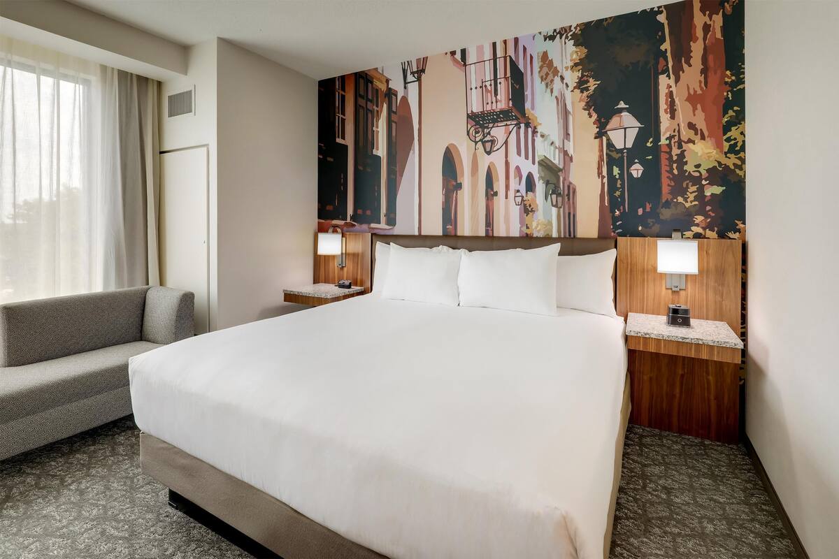 Une chambre d’hôtel avec un grand lit, un canapé, une table de chevet avec une lampe et une fresque murale.