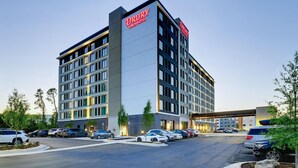Un hotel Drury Plaza con un diseño moderno, que presenta un letrero llamativo, varios pisos y un estacionamiento con varios coches.