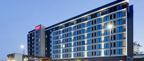 Ein mehrgeschossiges Hotel mit modernem Design, mit einer Reihe von Fenstern auf jeder Etage und einem Parkplatz davor.