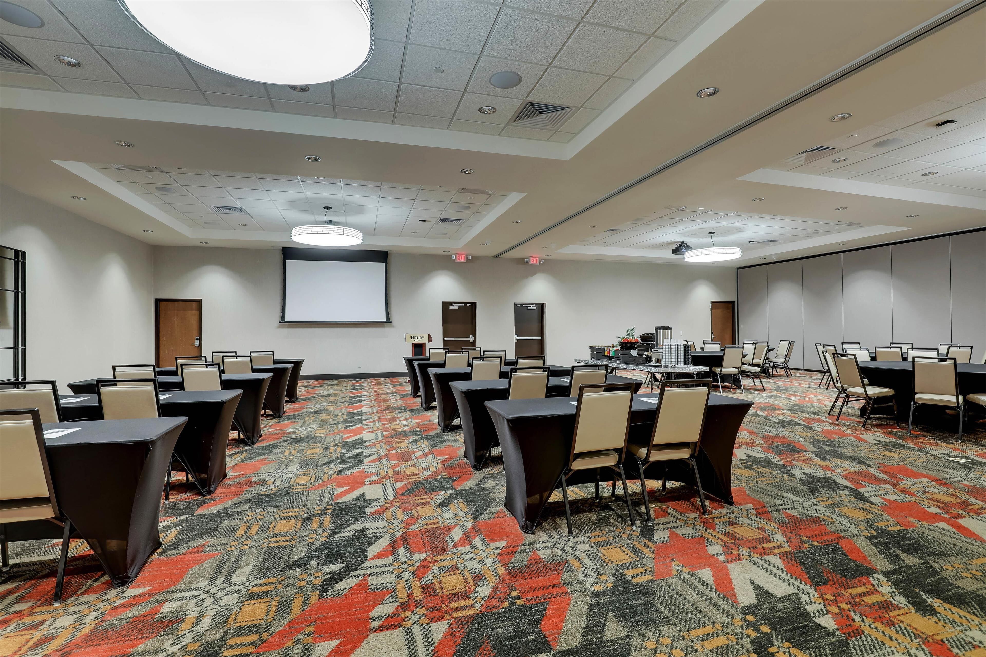 A conference room with multiple tables and chairs, a carpeted floor, and a projector screen.