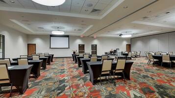 A conference room with multiple tables and chairs, a carpeted floor, and a projector screen.