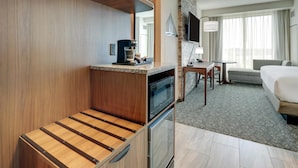 Habitación de hotel compacta con kitchenette, cama, zona de estar y un amplio ventanal.
