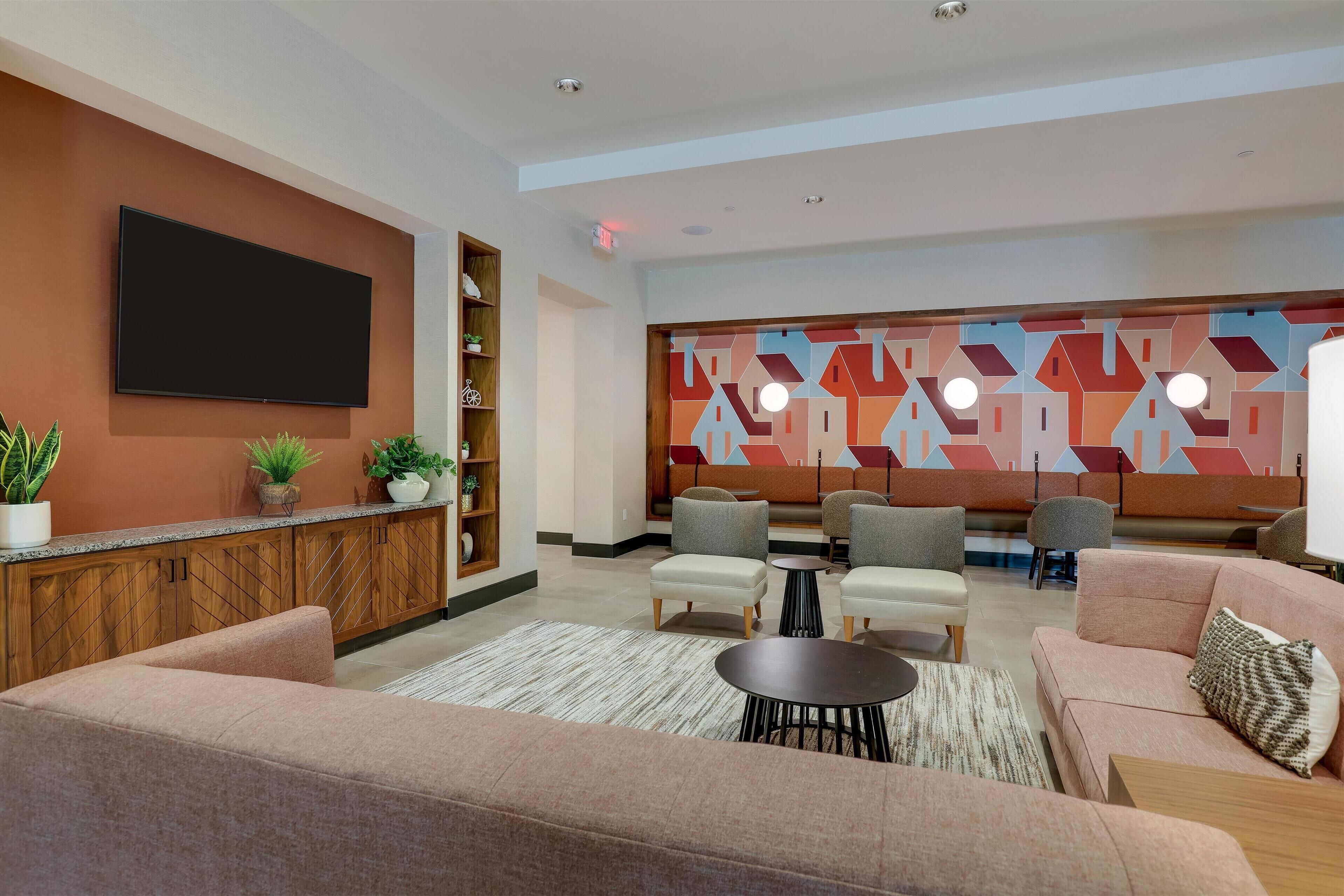 A modern living room with sofas, a coffee table, and a TV mounted on the wall. There are plants on the shelves and a colorful wall art piece.