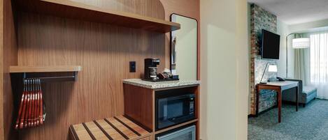 A compact hotel room with a kitchenette, a flat-screen TV, a small table, and a sofa.