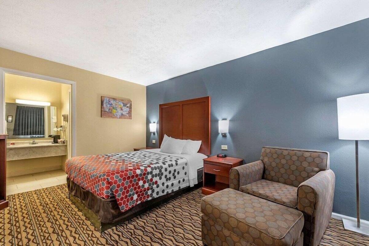 Quarto de hotel com cama, cadeira, escrivaninha e espelho.