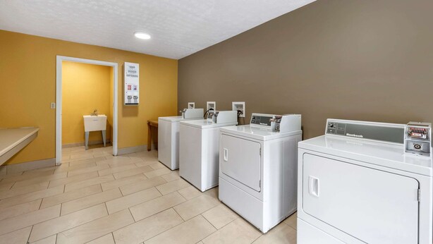 A laundry room with three white washing machines, a sink, and a sign indicating soap and bleach softeners. - Econo Lodge Erlanger - Cincinnati Airport (Erlanger)