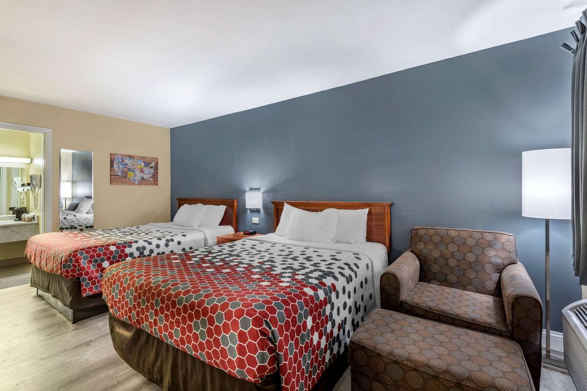Habitación de hotel con dos camas, una silla, una lámpara y un mapa en la pared.
