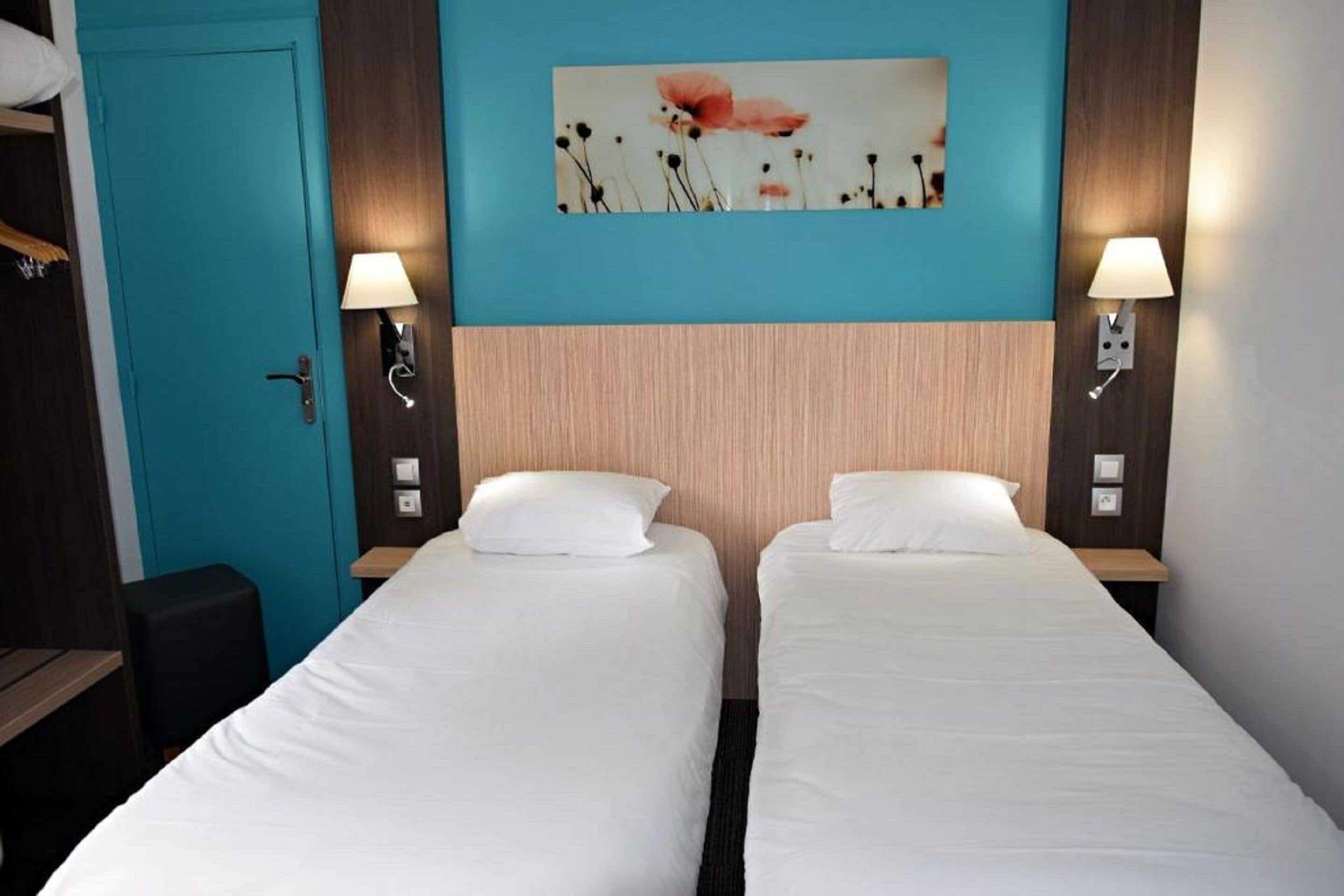 Habitación de hotel con dos camas individuales, una puerta color turquesa y un cuadro de flores colgado en la pared.