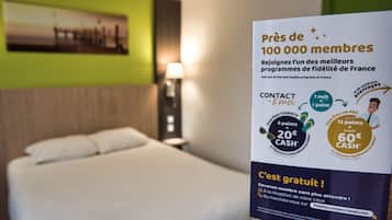 Une chambre d’hôtel avec un lit, une table de chevet et une affiche faisant la promotion d’un programme de fidélité.