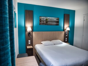 Ein Hotelzimmer mit einem großen Bett, zwei Nachttischen mit Lampen, einem Wandbild und einer Wand in Türkis.