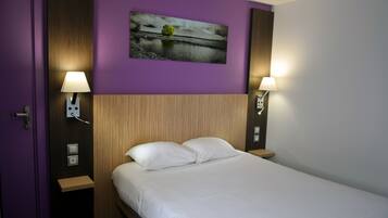 Habitación de hotel con cama, dos lámparas de noche, un cuadro en la pared y una puerta.