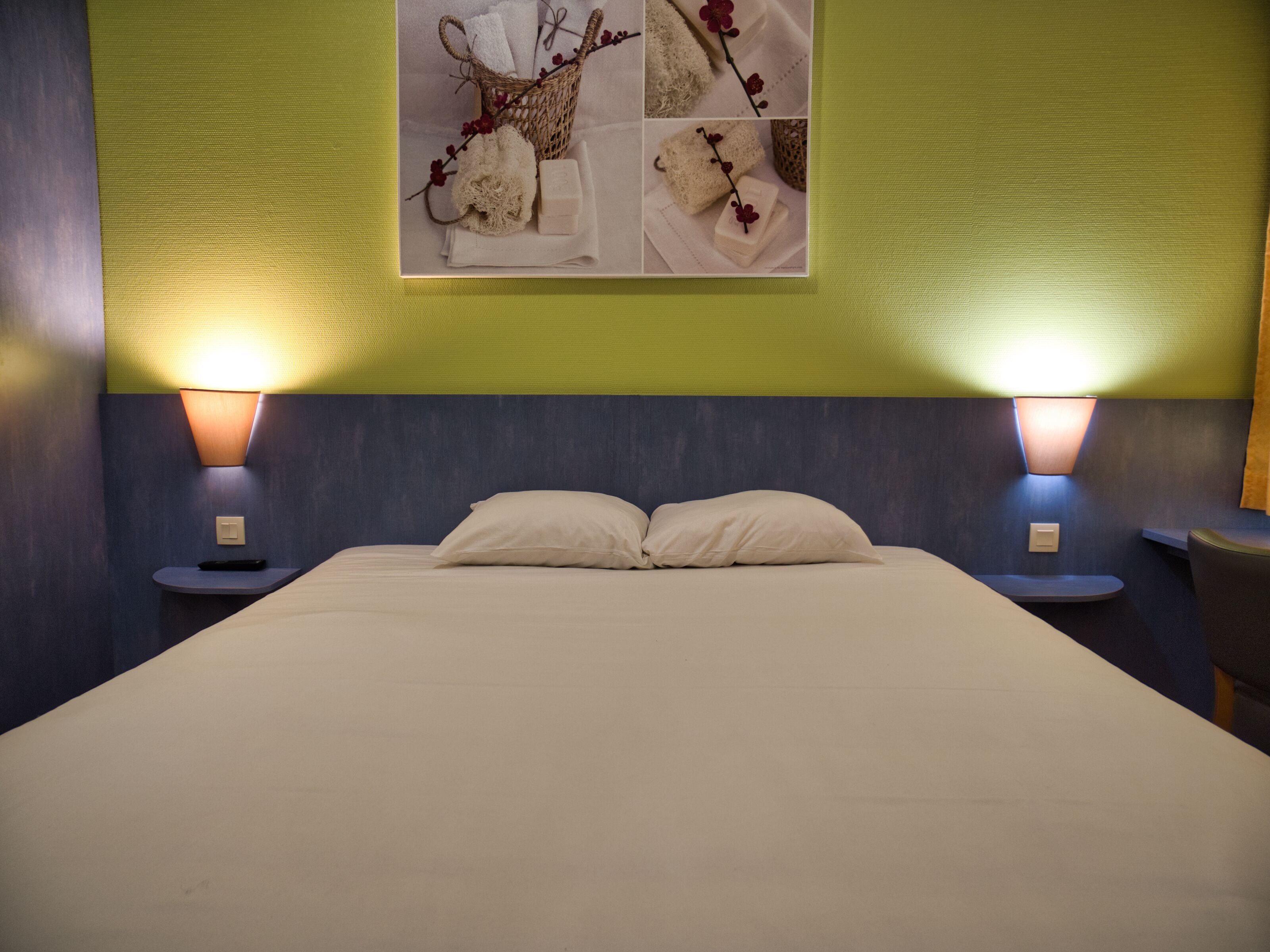 A neatly made bed with two pillows, flanked by two bedside tables with lamps, in a room with green walls and a large artwork above the bed.