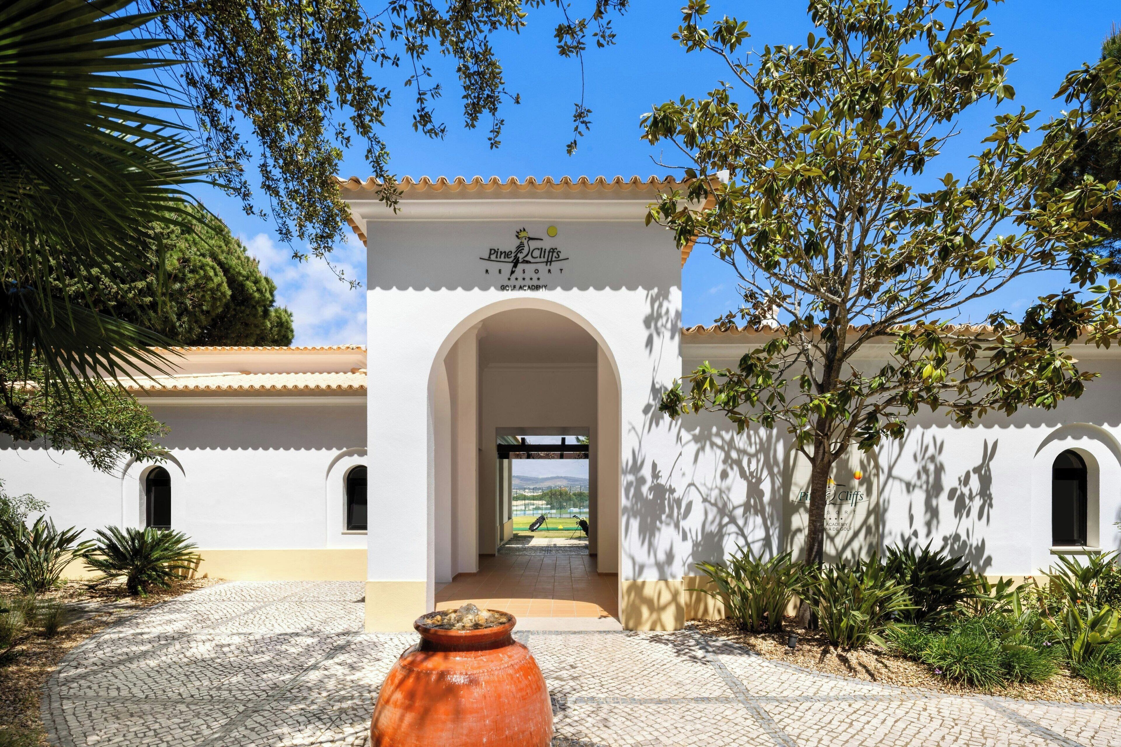 A white building with a sign reading "Pine Cliffs Resort" and an archway leading to a courtyard.