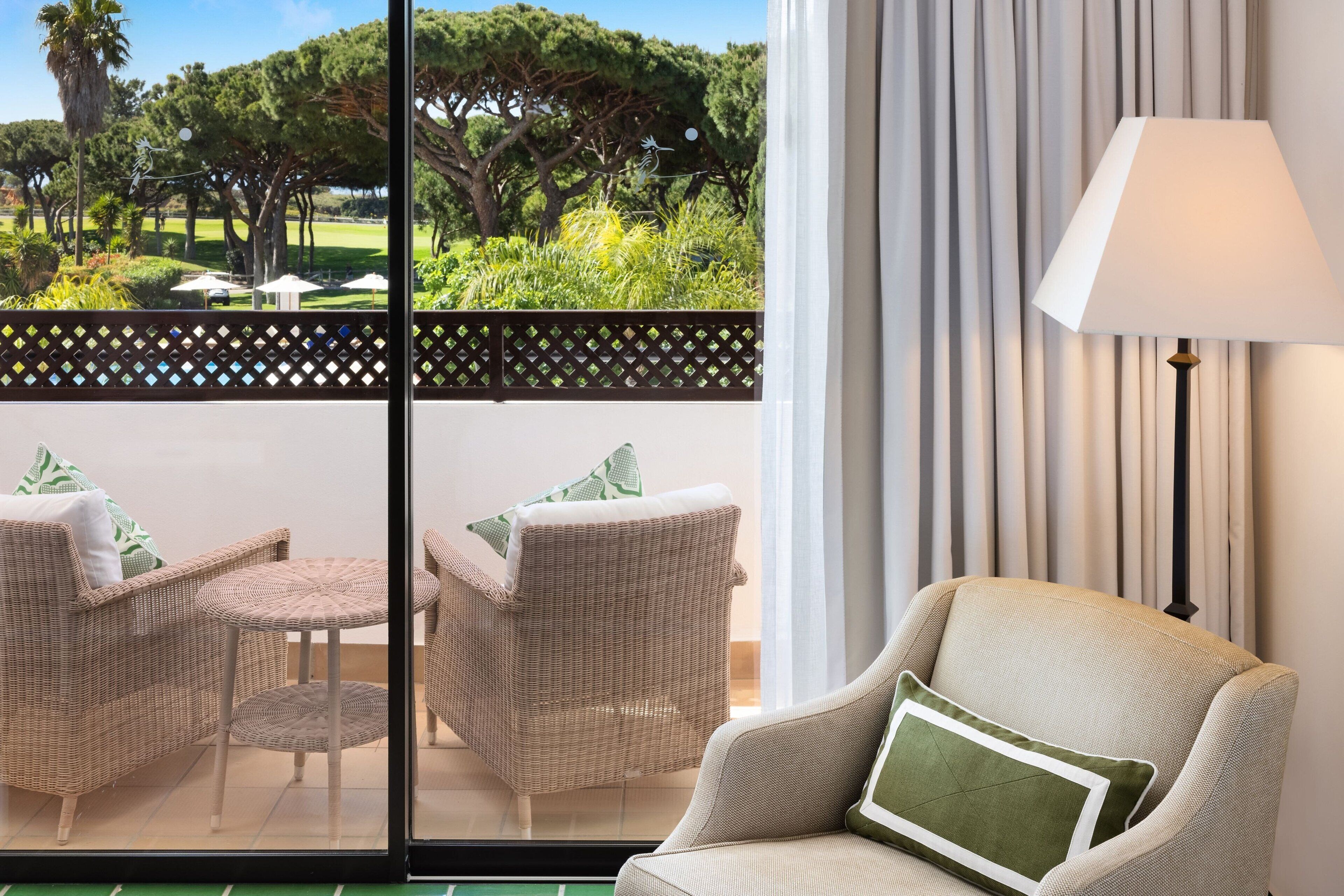 A room with a view of a golf course, wicker furniture, and a lamp.