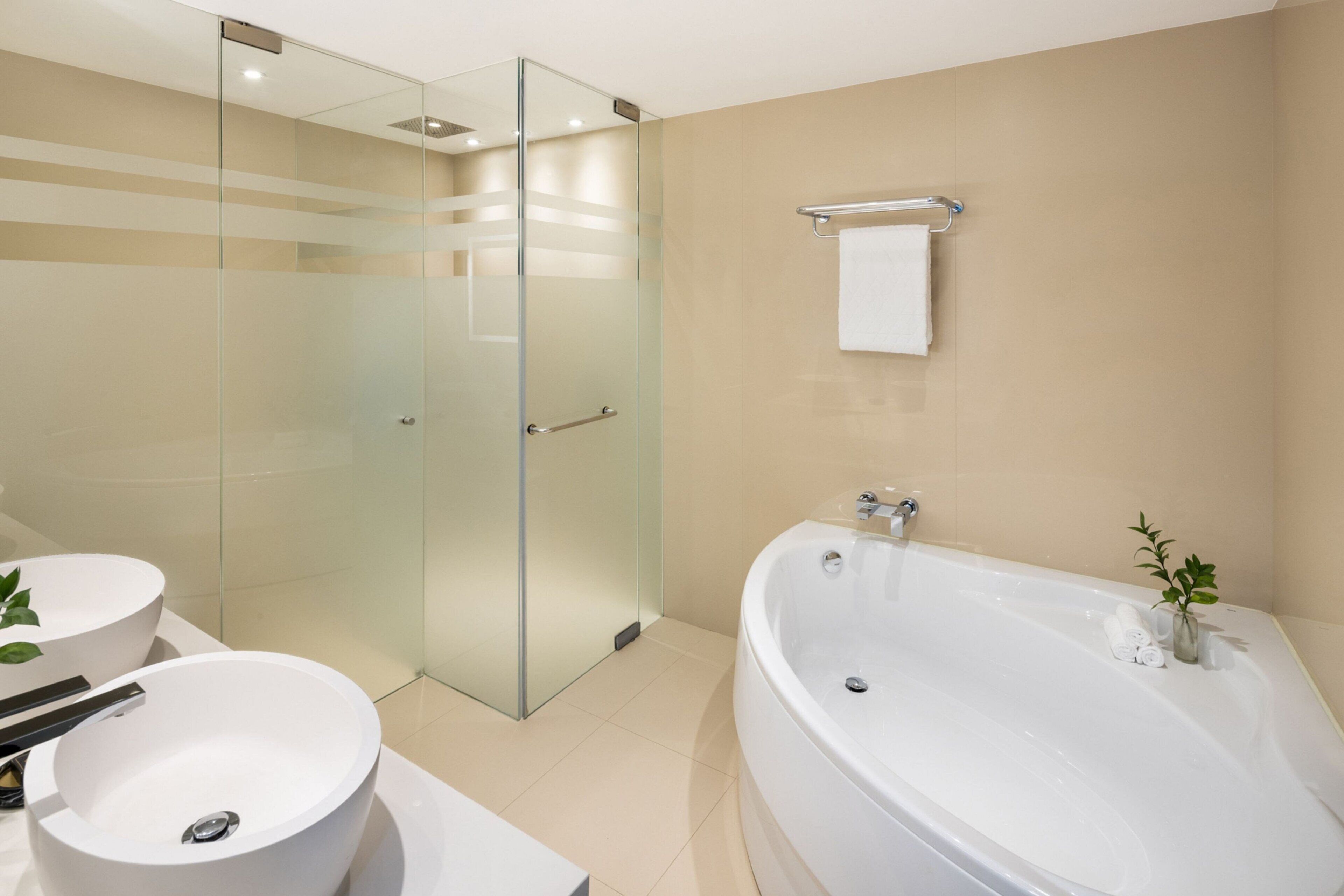 A modern bathroom with a glass shower enclosure, a large bathtub, and two sinks.