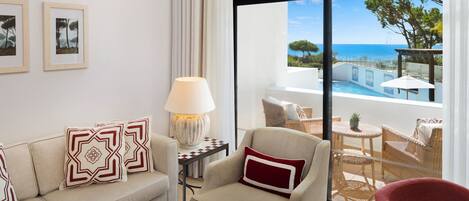 A modern hotel room with a sofa, armchair, and a view of the sea through large windows.