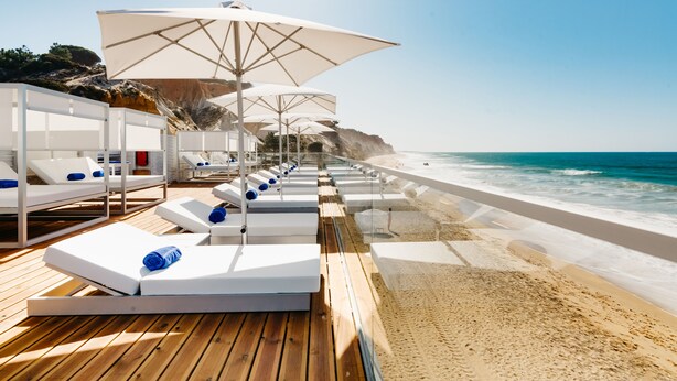 A beachside lounge area with white sunbeds and umbrellas, overlooking the ocean. - Pine Cliffs Hotel, a Luxury Collection Resort, Algarve (Albufeira)