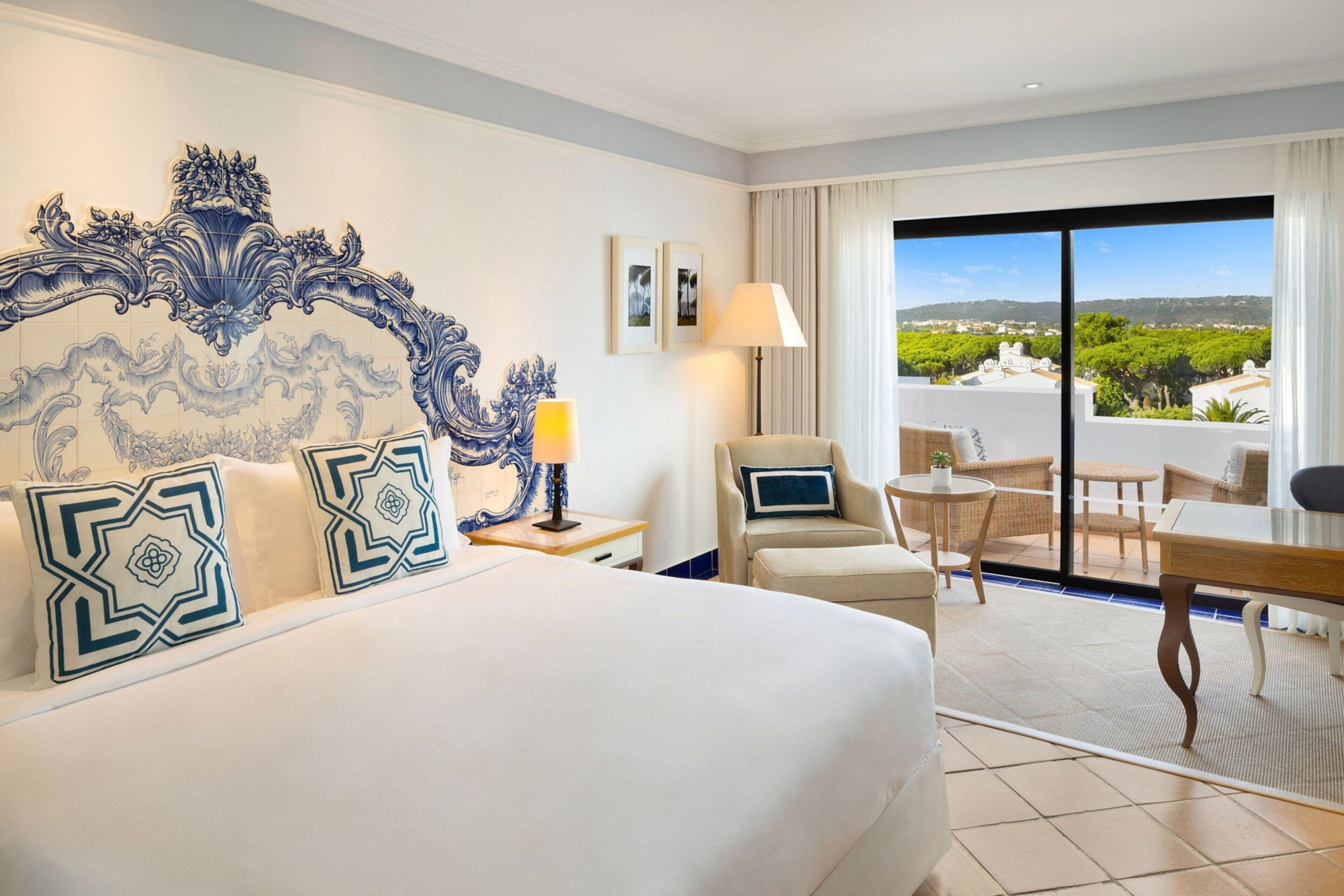Habitación de hotel con una cama grande, una silla, una mesita y un balcón con vistas.