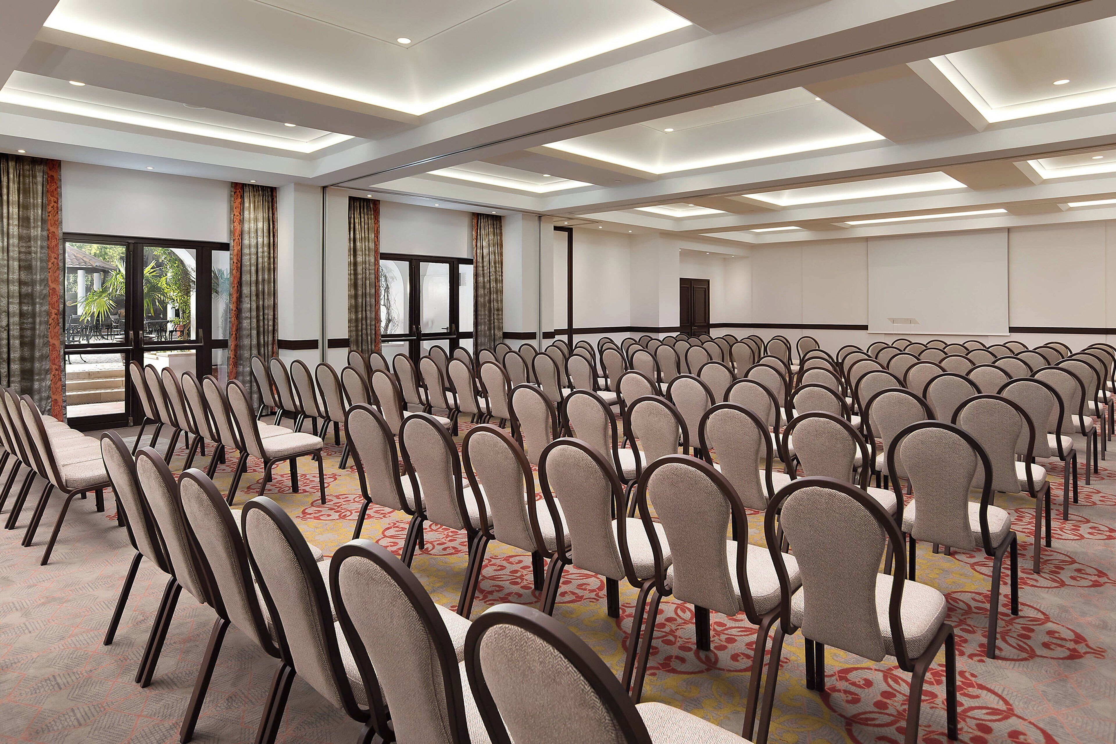 A conference room with rows of chairs, large windows, and a carpeted floor.