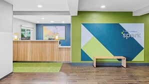 A reception area with a wooden desk, a green wall with a geometric design, and a bench. - Spark by Hilton Brunswick (Brunswick)