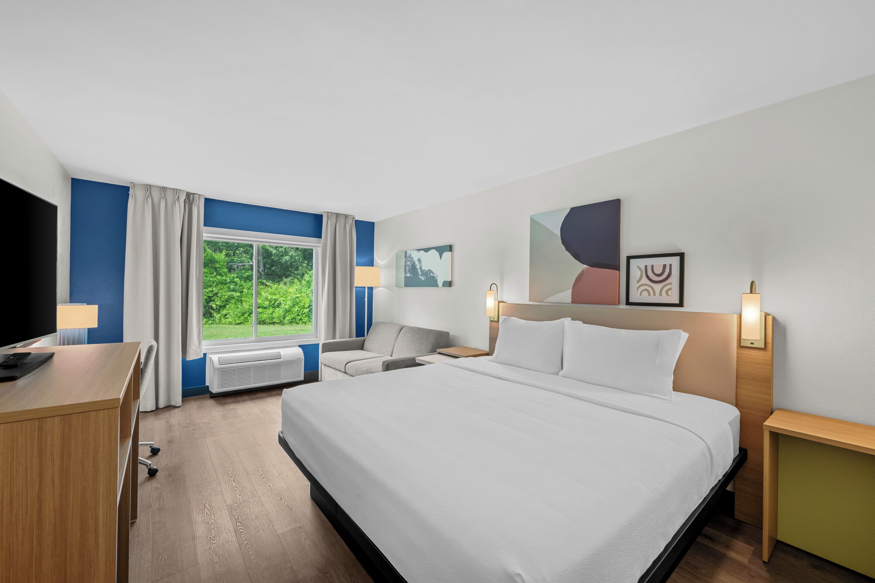Een hotelkamer met een bed, bureau, stoel en een raam met gordijnen.