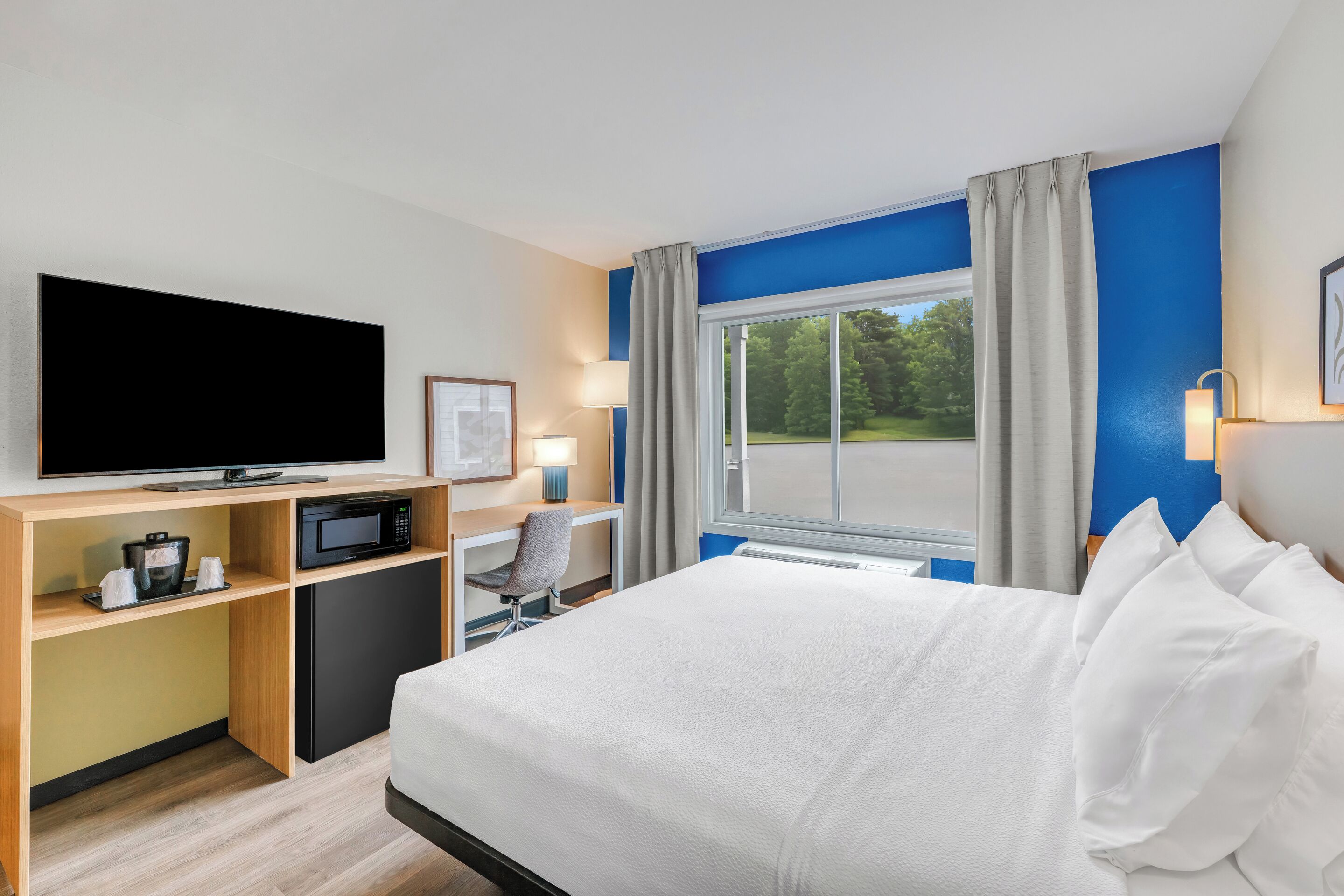A hotel room with a bed, a desk with a computer, a television, and a window with curtains.
