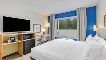 A hotel room with a bed, a desk with a computer, a television, and a window with curtains.