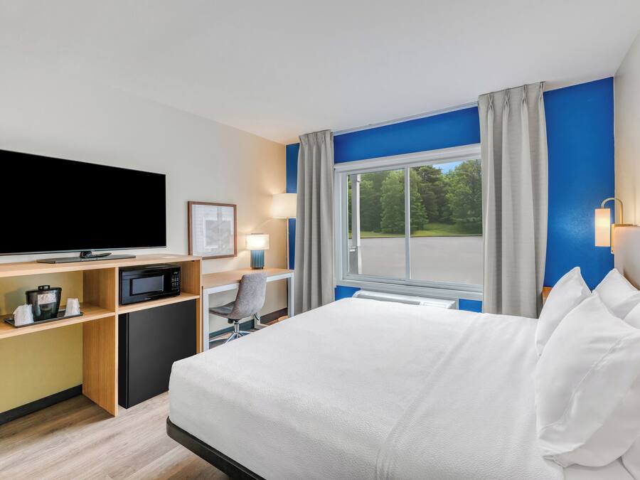 A hotel room with a bed, a desk with a computer, a television, and a window with curtains.